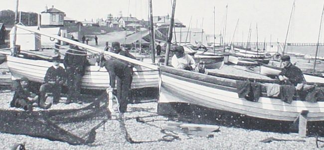 Fishermen in thick jerseys by their fishing boats on a shore crowded with small boats in front of a shallow hill